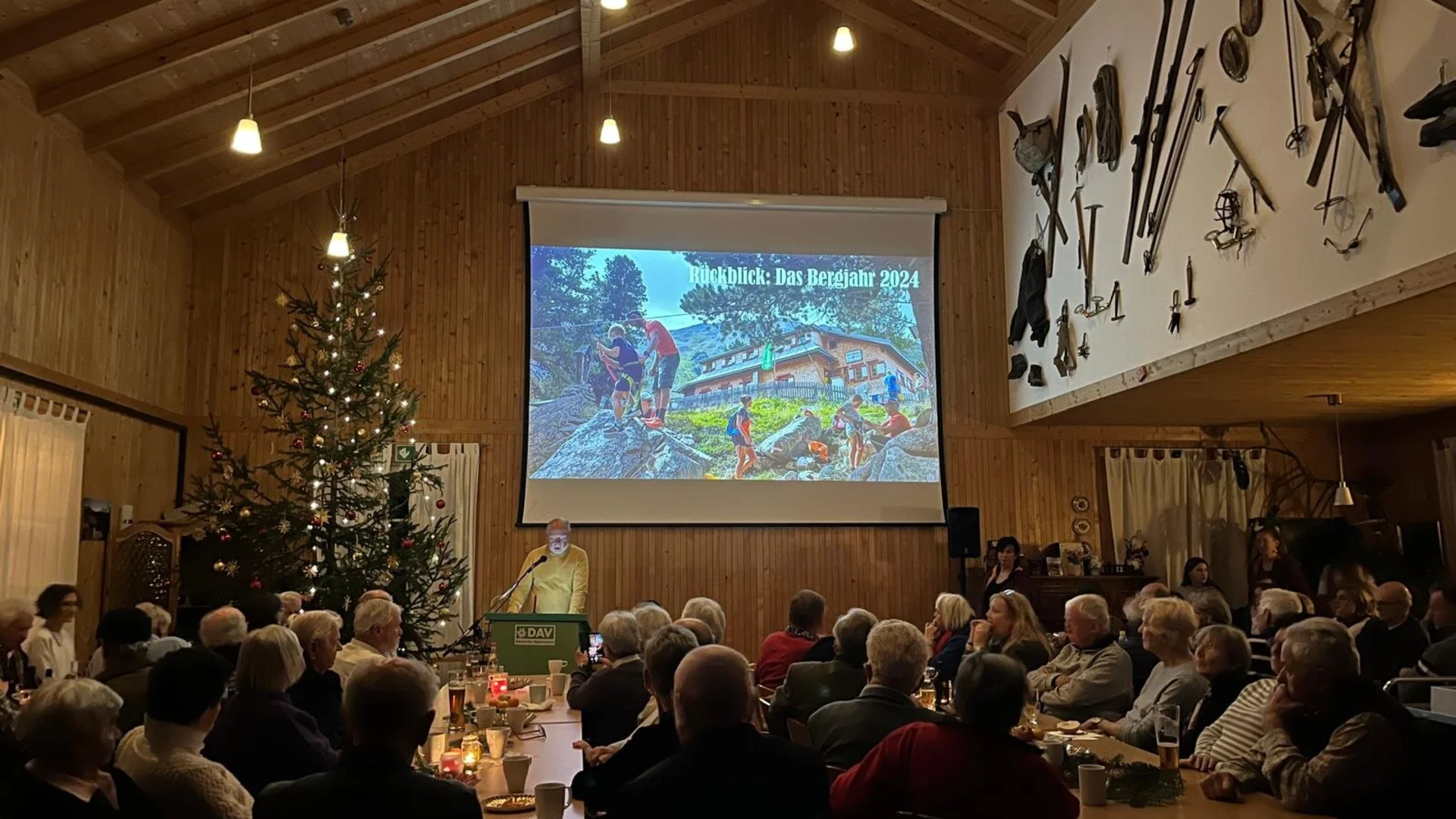 Foto der Versammlung im gefüllten Saal mit Beemer und Weihnachtsbaum Weihnachtsfeier 2024 | © DAV Starnberg