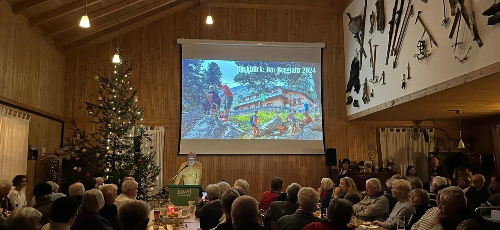 Foto der Versammlung im gefüllten Saal mit Beemer und Weihnachtsbaum Weihnachtsfeier 2024 | © DAV Starnberg