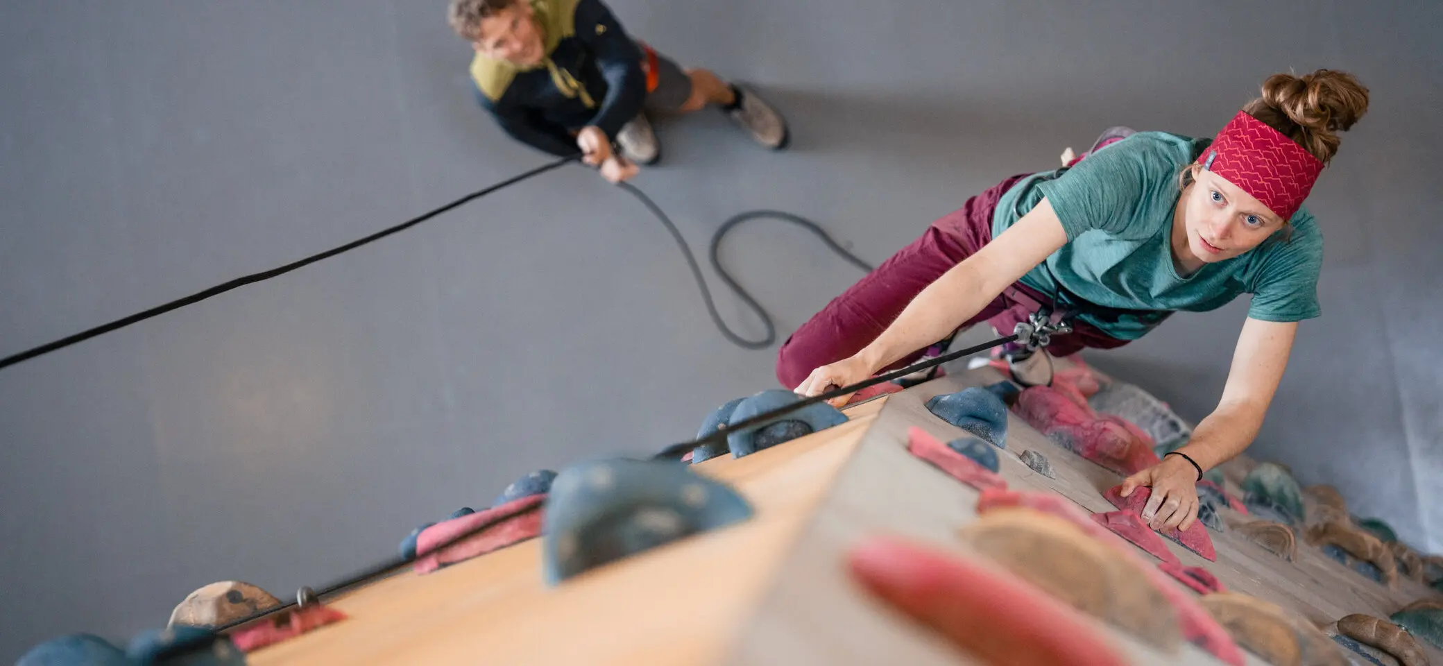 Eine Frau klettert in einer Kletterhalle, ihr Partner sichert sie. | © DAV / Julian Rohn